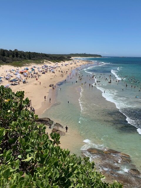 Caves Beach on a busy summer day with people enjoying the sand and surf