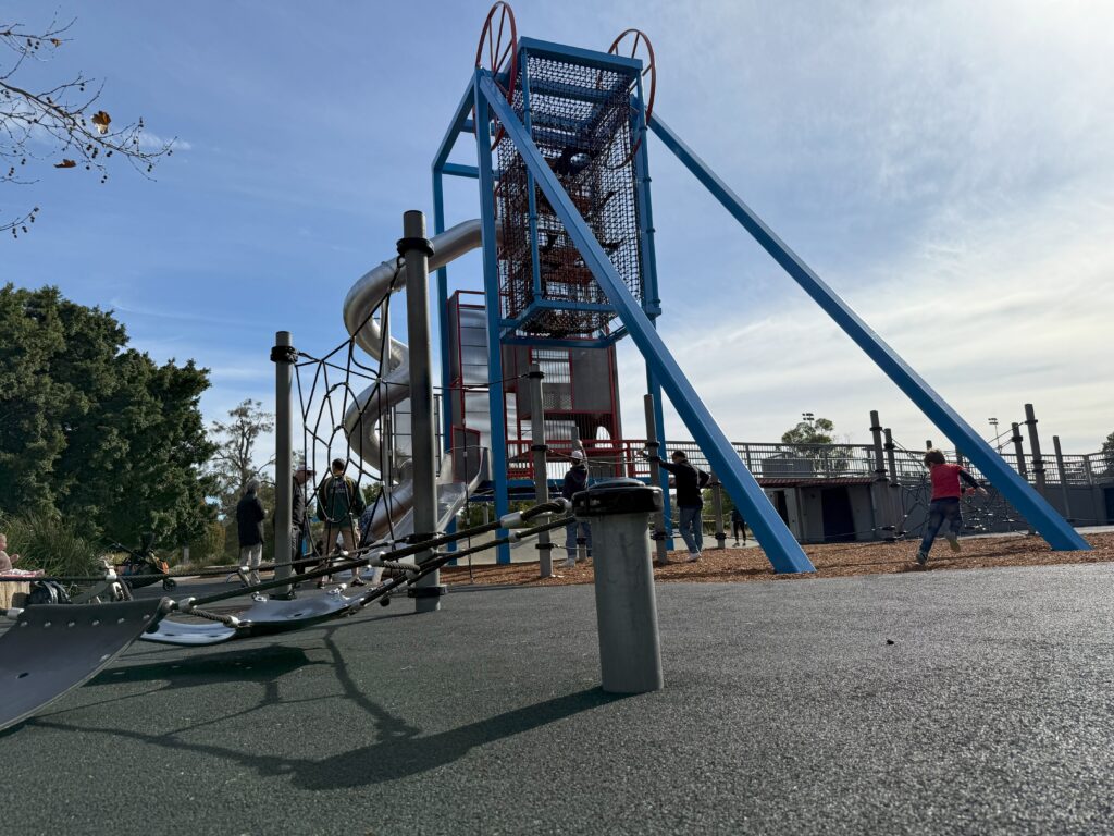 Kids climbing the huge playground and sliding down the aluminium tube slippery dip at Speers Point Park in Lake Macquarie