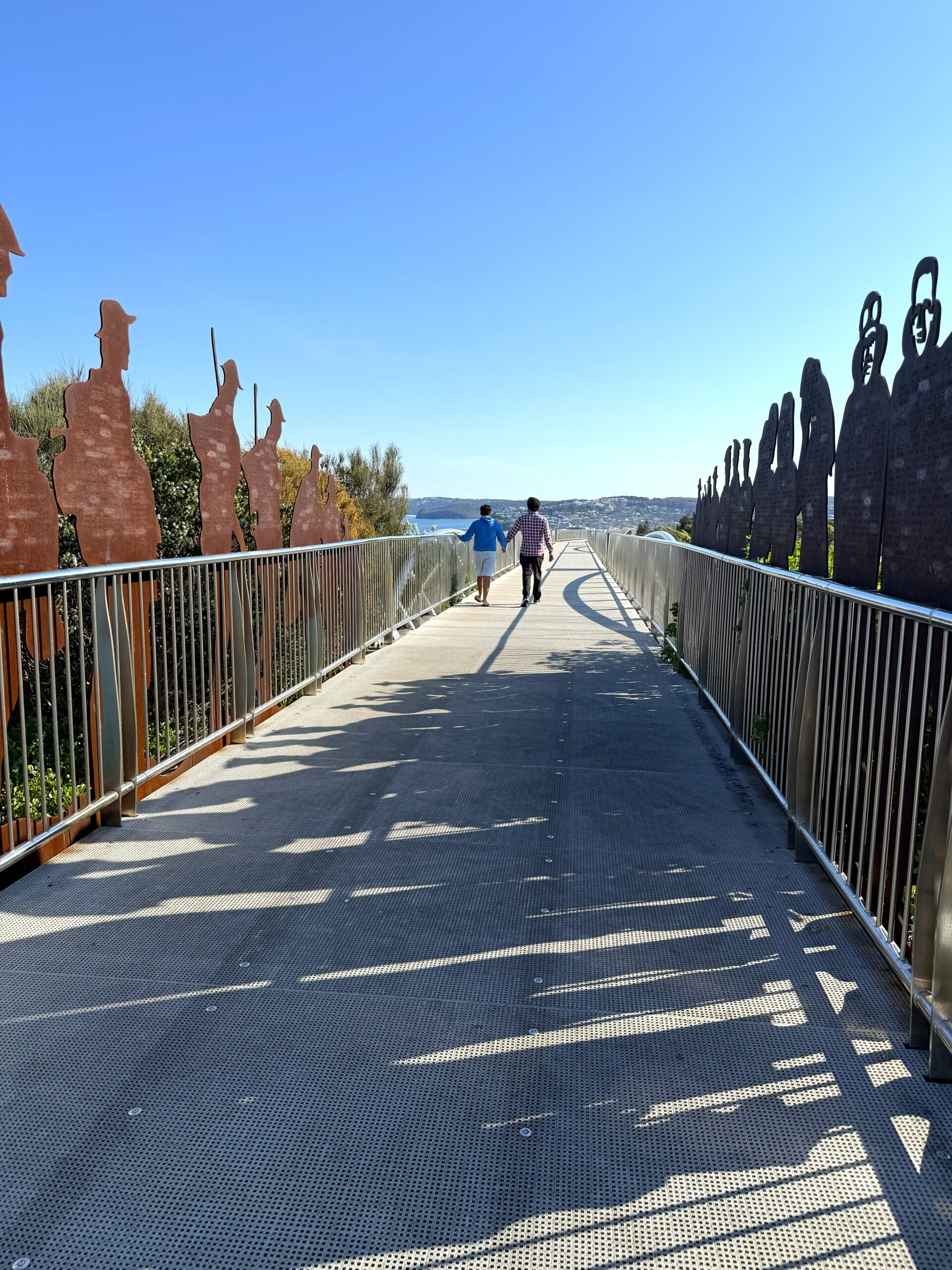 Two people walking along the ANZAC Memorial Walk through the steel digger sentries lining the path, Newcastle