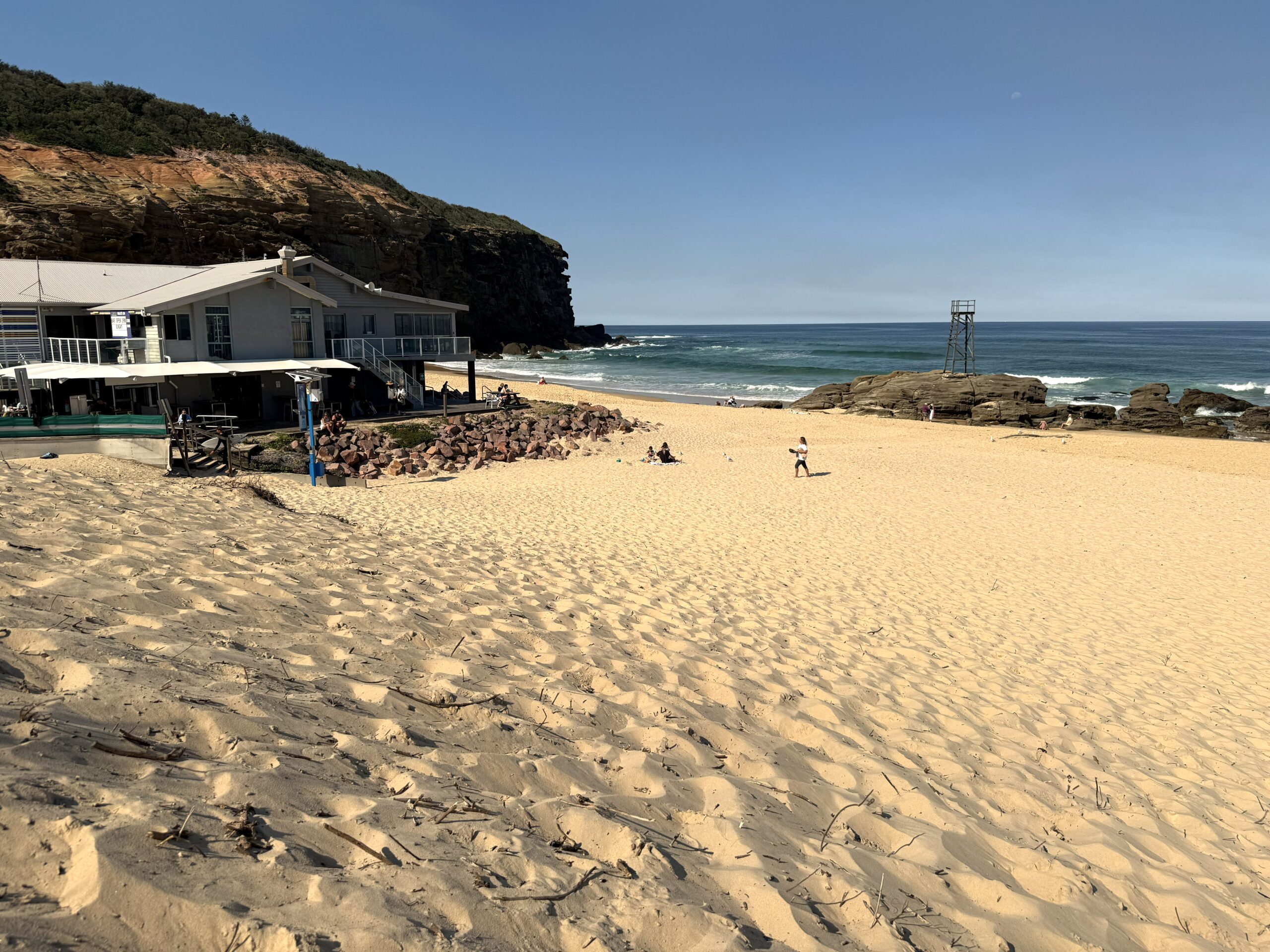 Looking across golden sands towards the surf club, historic shark lookout towers and red cliffs at Redhead Beach, Lake Macquarie