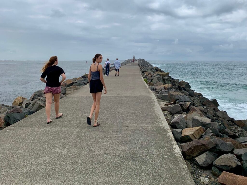 2 girls walking along Nobbys break wall looking for coal ships