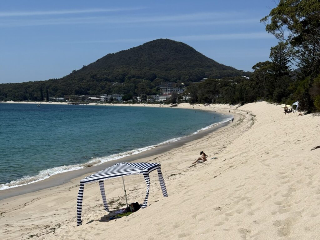 Families enjoying a day in the sunshine on the white sands of Shoal Bay. Tomaree Headland stands int he background.