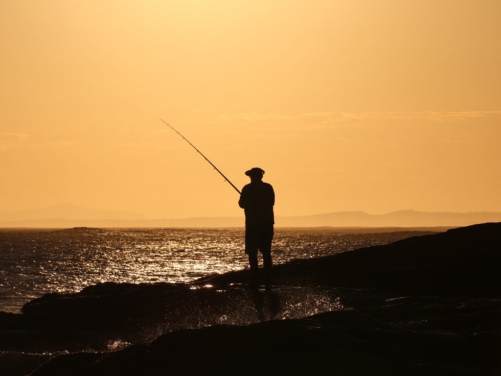 A man fishing from the rocks at Birubi Point as the sunsets