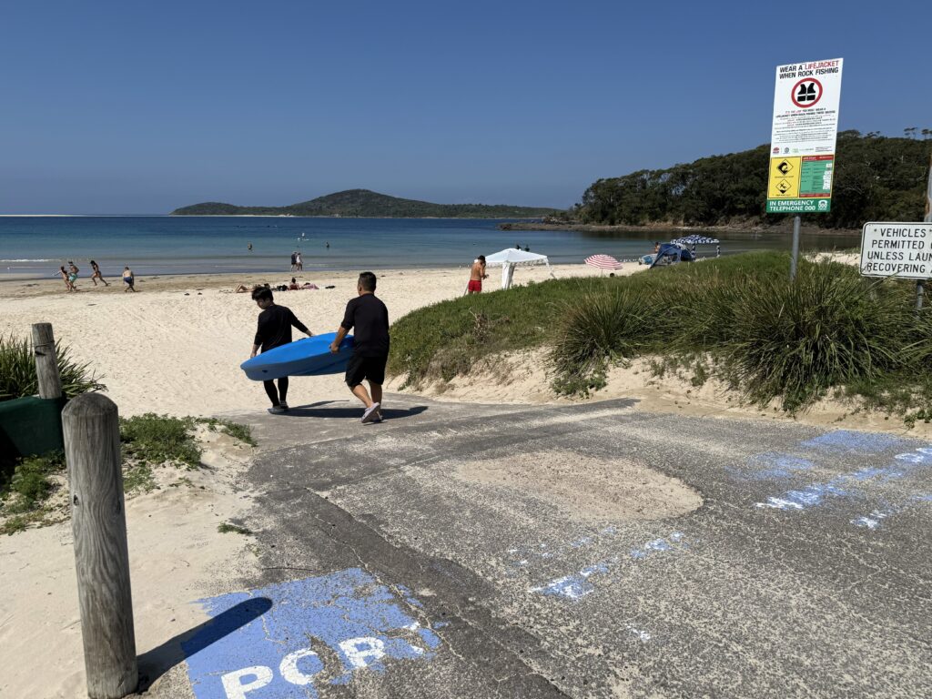 2 Kayakers using the Fingal Beach boat access ramp to carry their kayak onto the sand on a perfect sunny day