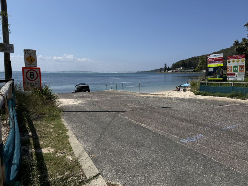 Shoal Bay Boat Ramp with car retrieving boat with Tomaree Headland in the background indicating close proximity to the Port Stephens Heads.