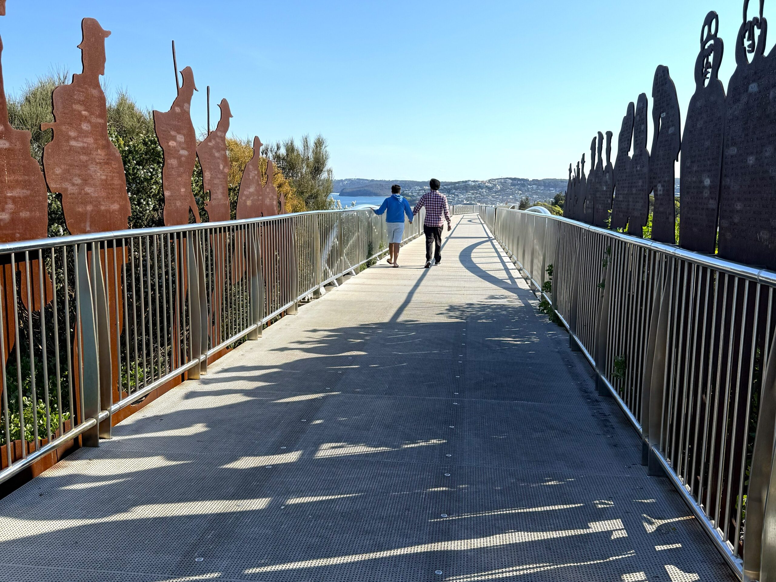 Two people walking along the ANZAC Memorial Walk through the steel digger sentries lining the path, Newcastle