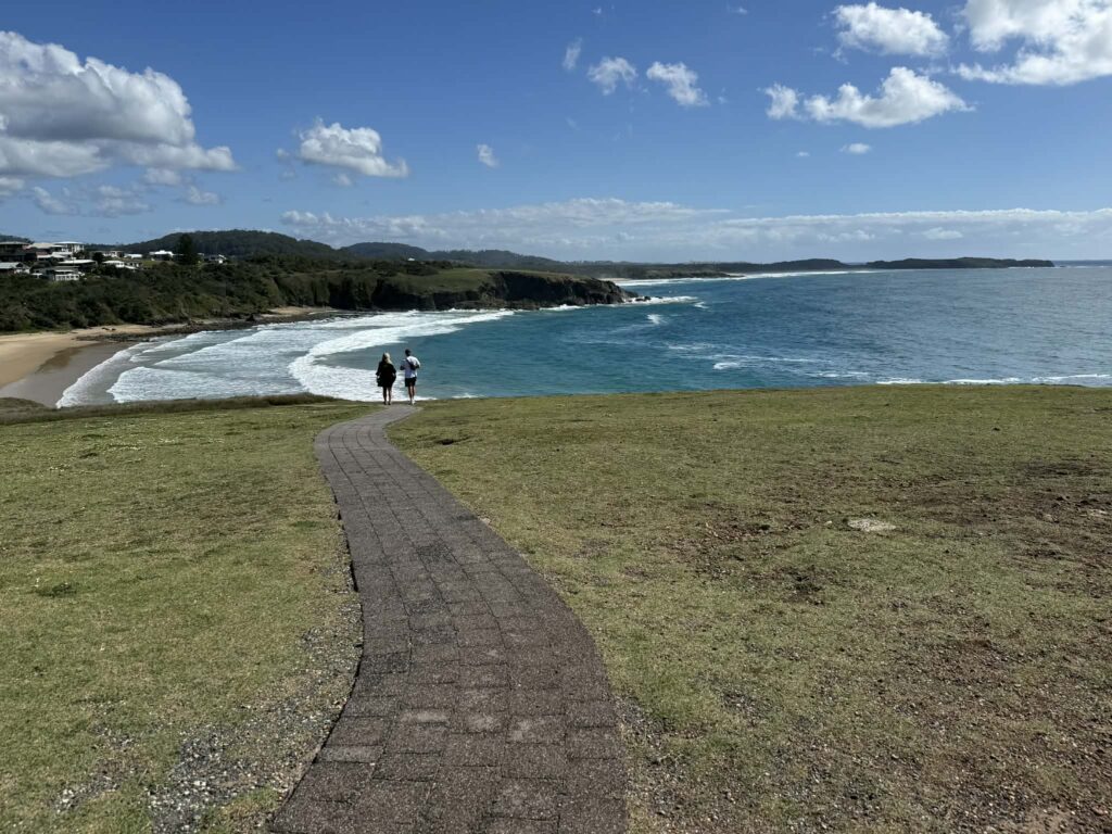 A couple enjoying stunning coastal views walking along the accessible walking track on Look at Me Now Headland towards Shelly Beach after whale watching in Coffs Harbour