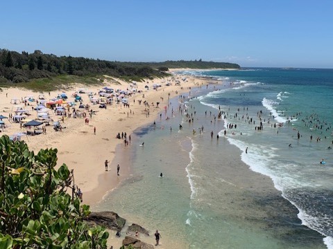 Crowds swimming in the crystal clear surf between the flags at Caves Beach. Lake Macquarie on a perfect summer day as seen from the cliff top
