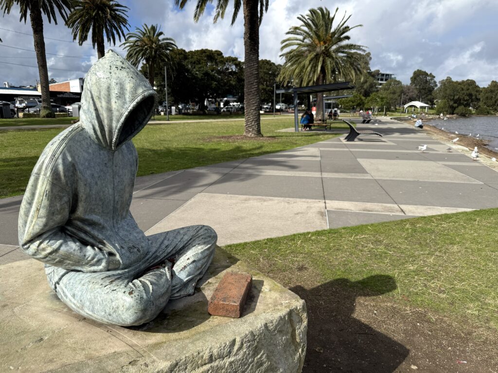 Sculpture of a person in hoodie sitting looking out to Lake Macquarie from Warners Bay foreshore on a stormy day