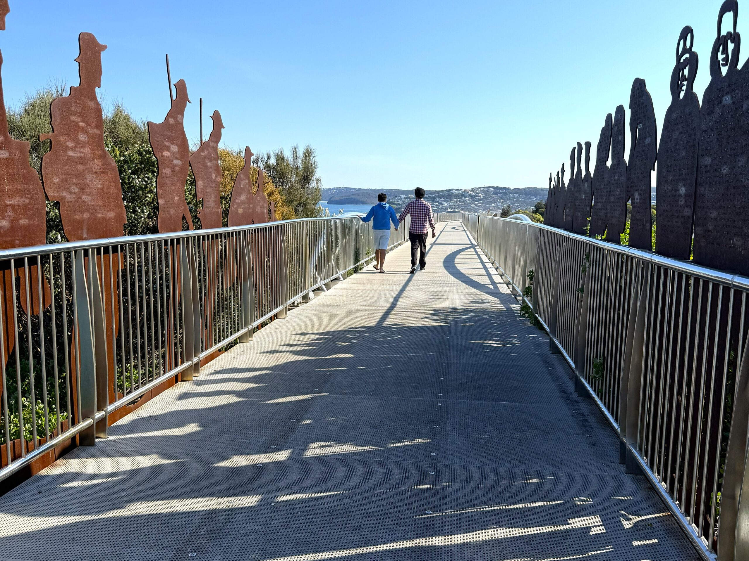 Two people walking along the ANZAC Memorial Walk through the steel digger sentries lining the path, Newcastle
