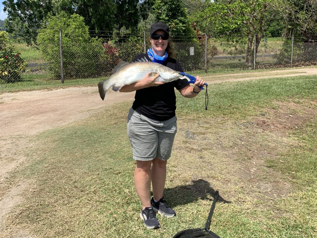 A woman stands proudly holding a large Barramundi caught at Hook-a-Barra.