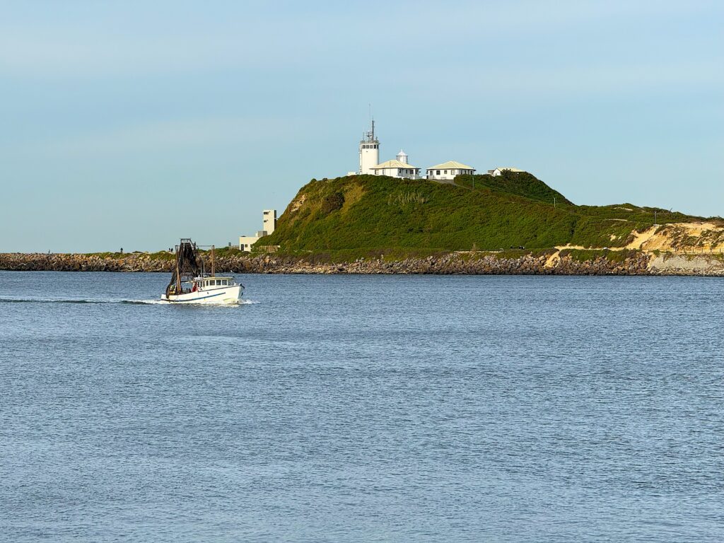 A white fishing vessel enters Newcastle Harbour overlooked by Nobbys Lighthouse - as seen from the Shipwreck Walk