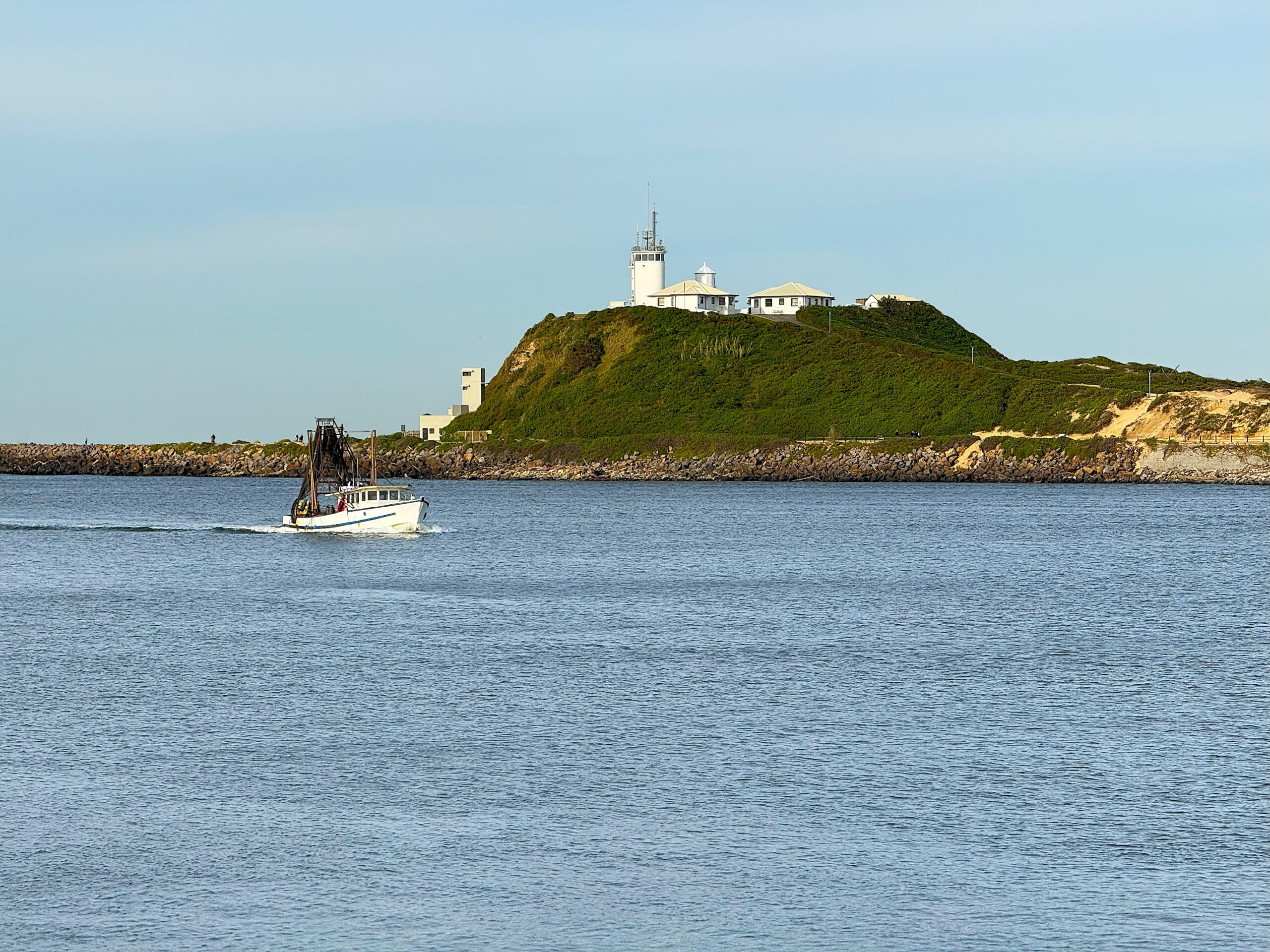 A white fishing vessel enters Newcastle Harbour overlooked by Nobbys Lighthouse - as seen from the Shipwreck Walk