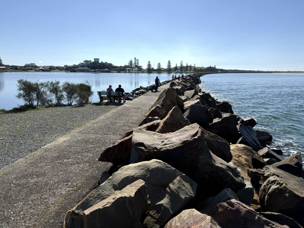 People enjoying the sunshine with a stroll along the Harrington Breakwall. The township of Harrington is in the distance.