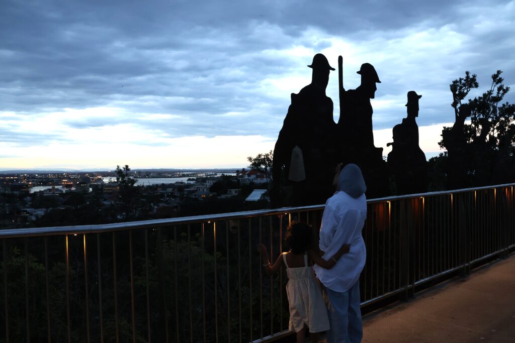 Mother and daughter read the names of fallen soldiers killed at war on the ANZAC Memorial Walk with views of Newcastle City at sunset