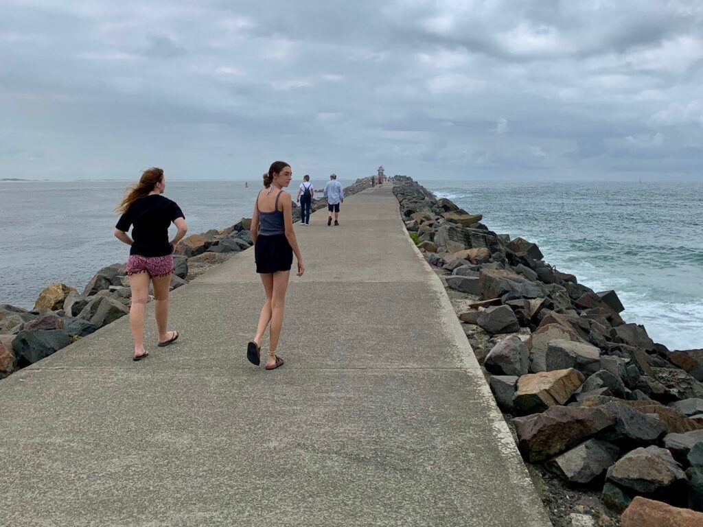 2 girls walking along Nobbys break wall looking for coal ships