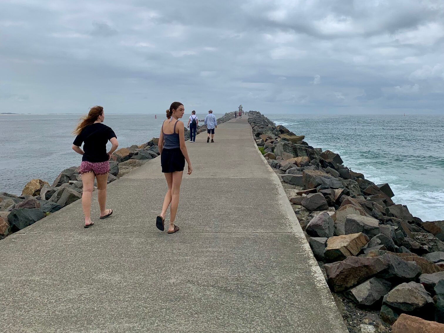 2 girls walking along Nobbys break wall looking for coal ships