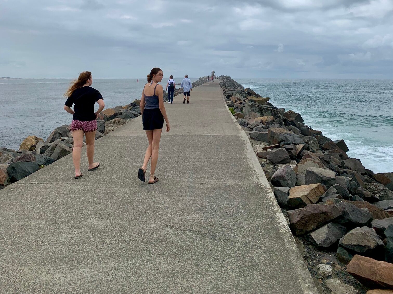 2 girls walking along Nobbys break wall looking for coal ships