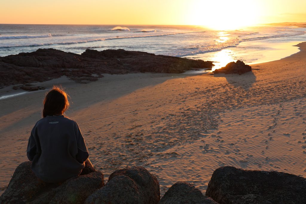 Girl sitting on the rocks watching the sun set over Birubi Beach