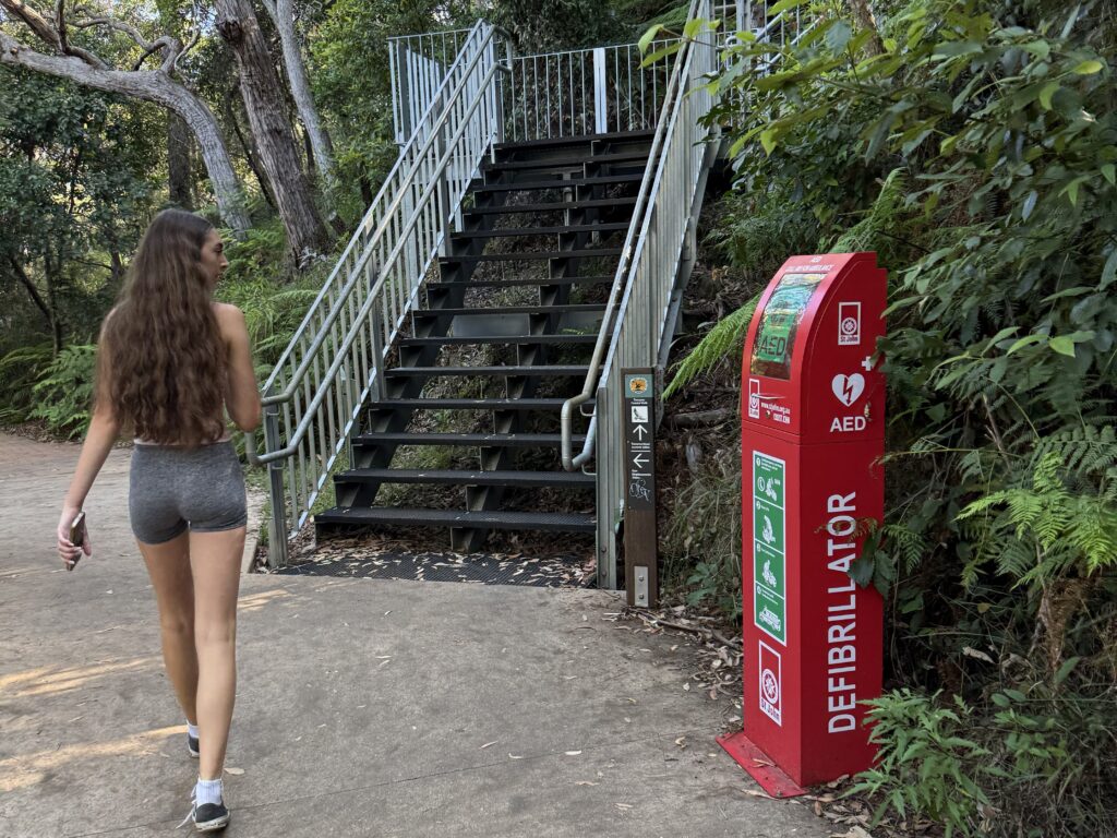 Girl walks towards the metal stairs on the Tomaree Headland Summit Walk looking anxiously at the defibrillator
